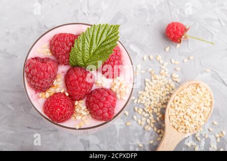 Joghurt mit Himbeere und Sesam in Glas und Holzlöffel auf grauem Betongrund. Draufsicht, flach liegend, Nahaufnahme. Stockfoto