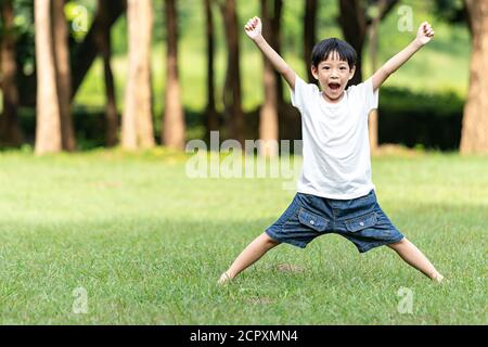 Portrait Asian junge, die Arme im öffentlichen Park. Das Kind hob beide Arme vor Freude. Lebensleistungen und Erfolgskonzept. Stockfoto