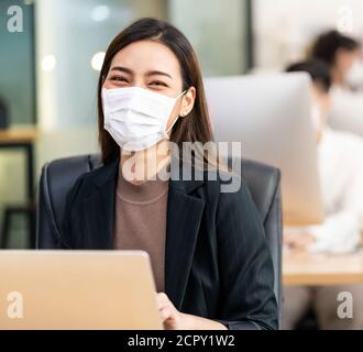 Portrait der asiatischen Büroangestellte Geschäftsfrau tragen Schutzmaske Arbeiten Sie in einem neuen normalen Büro mit interracial Kollegen im Hintergrund Als sozial Stockfoto