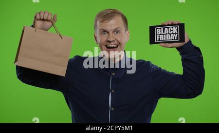 Glückliche fröhliche Emotionen des Store man Client. Überraschte Kerl zeigt Einkaufstaschen und Black Friday Inschrift, Blick erstaunt über niedrige Kosten Kauf, Rabatt. Chroma-Taste Hintergrund. 6k Downscale Stockfoto