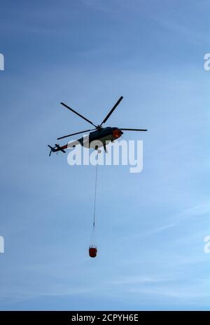 MIL Mi-17 Hubschrauber fliegt in den Himmel mit Eimer Löschwasser Stockfoto