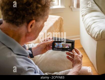 Älterer Mann beim Streaming des jüdischen Neujahrs Rosh Hashanah Morgendienstes auf seinem Smartphone; Rabbi auf der linken Seite des Bildschirms und Kantor auf dem Stockfoto