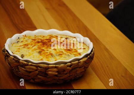 Blumenkohl mit Bechamelsauce und geschmolzenem Käse darauf Keramikschale mit Strohmattenabdeckung Stockfoto