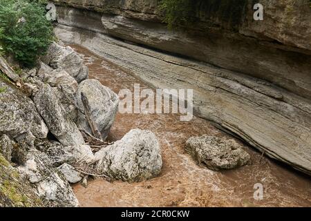 Bergschlucht mit Steinen, die in einen schlammigen Fluss fielen Bei Überschwemmungen nach Regen Stockfoto