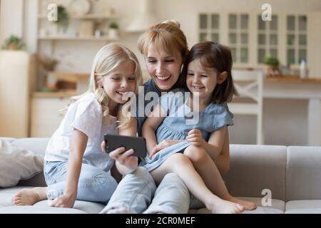 Positive Mutter und Töchter mit Handy, um Cartoons zusammen zu sehen Stockfoto