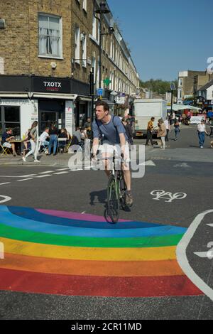 Besucher des Broadway Market radeln auf verkehrsfreien Straßen mit Straße Schilder, die darauf hinweisen, dass die soziale Distanz wegen Coronavirus sicher gehalten werden sollte / Covid-19 Pandemie in Hackney, London, England, Großbritannien Stockfoto