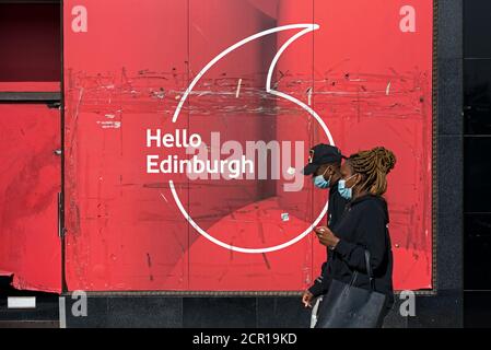 Junges farbiges Paar mit Gesichtsmasken beim Gang durch den geschlossenen Vodaphone-Laden in der Princes Street, Edinburgh, Schottland, Großbritannien. Stockfoto