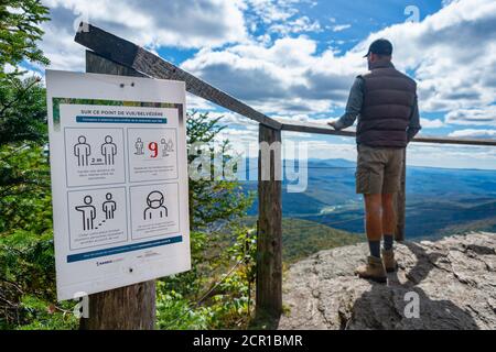 Sutton, CA - 17. September 2020: Mann, der die Aussicht auf den Gipfel des Mount Sutton neben einem Sicherheitsschild covid-19 betrachtet Stockfoto