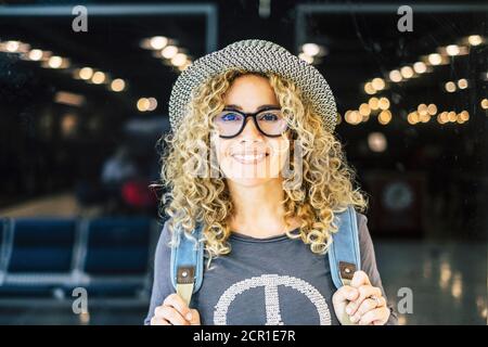 Porträt und Nahaufnahme der schönen lockigen und blonden Frau Blick auf die Kamera lächelnd - glückliche Menschen auf dem Flughafen reisen - Urlaub im Freien Stockfoto