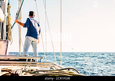 Segelaktivität Menschen - Mann von hinten gesehen Steh auf dem Deck eines Segelbootes und schaue auf den Horizont und den blauen Ozean und Himmel Stockfoto