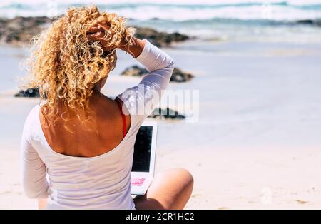 Digitaler Nomade glücklicher Lifestyle und Menschen clever arbeiten überall mit Roaming und Verbindungstechnik - schöne blonde lockige Frau an Der Strand w Stockfoto
