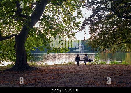 Zwei Leute sitzen auf einer Bank unter Buchen und reden In einem Münchner Park im September Stockfoto