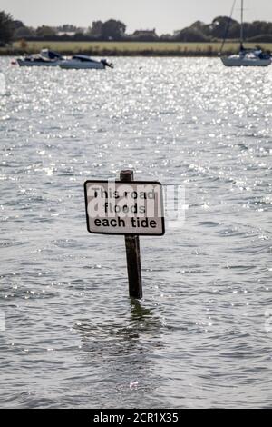 Ein Schild mit der Aufschrift "Diese Straße überflutet jede Flut", das teilweise bei Flut im historischen Dorf Bosham, West Sussex, Großbritannien, untergetaucht ist. Stockfoto