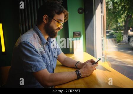 Mann hält Telefon und chattet online sitzen in einem Café Stockfoto