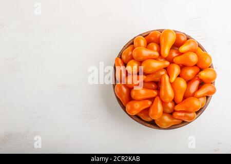Frische orangefarbene Traubentomaten in Holzschüssel auf weißem Holzhintergrund. Draufsicht, flach liegend, Kopierraum. Stockfoto