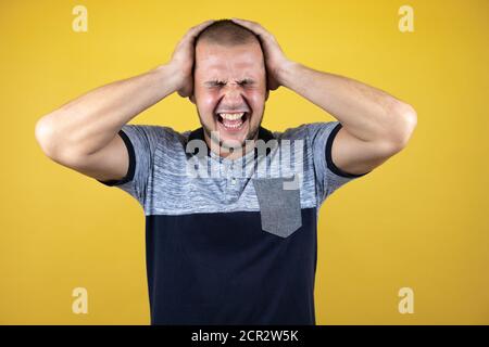 Russischer Mann, der über einem versohlten gelben Hintergrund stand und unter Kopfschmerzen litt Verzweifelt und gestresst, weil Schmerzen und Migräne mit ihren Händen Am Kopf Stockfoto