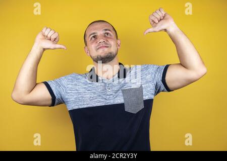 Russischer Mann, der über einem versohlten gelben Hintergrund steht und selbstbewusst mit einem Lächeln auf dem Gesicht aussieht und sich mit stolzen und glücklichen Fingern zeigt. Stockfoto