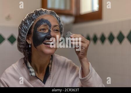 Nahaufnahme einer lächelnden Frau beim Entfernen der Schlammmaske Von ihrem Gesicht Stockfoto