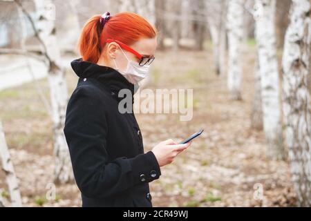 Maskiertes Mädchen schaut am Telefon und liest Nachrichten über Epidemie. Schutz vor Viren-Konzept mit Kopierplatz. Stockfoto