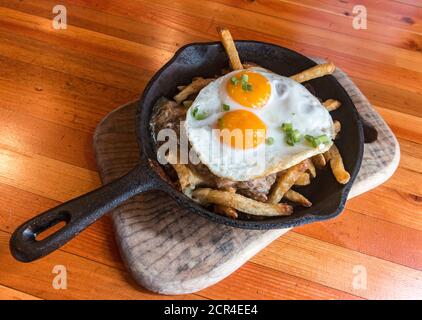 Fraser Valley Poutine mit Entenconfit, Käsequark, Pommes Frites und garniert mit zwei sunnyside up Eier. Präsentiert in einer kleinen gusseisernen Pfanne. Dies ist das typische Gericht im Edible Canada, einem Café auf Granville Island, British Columbia, Kanada. Stockfoto