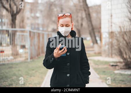 Maskiertes Mädchen schaut am Telefon und liest Nachrichten über Epidemie. Schutz vor Viren-Konzept. Stockfoto