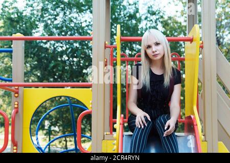 Schöne junge Frau sitzt auf Rutsche im Park und denken über etwas nach. Vergangener Kindheitsbegriff mit Kopierraum. Stockfoto