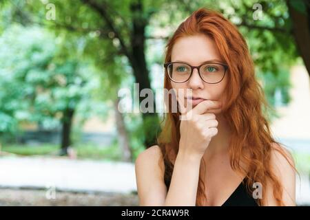 Nachdenklich junge Lehrerin in Brille geht im Park. Ingwer Mädchen suchen zur Seite. Lösung der wirtschaftlichen Probleme Konzept mit Kopierraum. Stockfoto