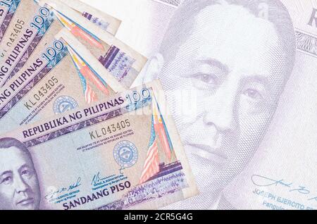 100 philippinische Piso-Scheine liegen im Stapel auf dem Hintergrund einer großen halbtransparenten Banknote. Abstrakter Geschäftshintergrund mit Kopierbereich Stockfoto