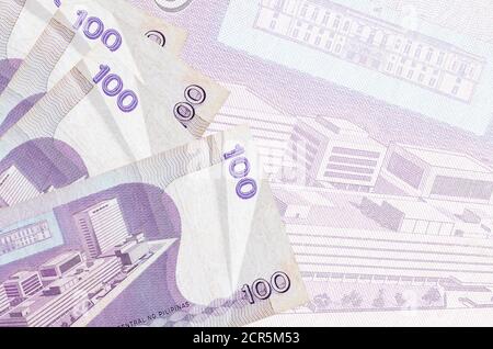 100 philippinische Piso-Scheine liegen im Stapel auf dem Hintergrund einer großen halbtransparenten Banknote. Abstrakter Geschäftshintergrund mit Kopierbereich Stockfoto