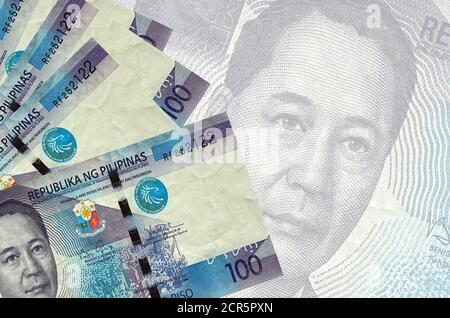 100 philippinische Piso-Scheine liegen im Stapel auf dem Hintergrund einer großen halbtransparenten Banknote. Abstrakter Geschäftshintergrund mit Kopierbereich Stockfoto