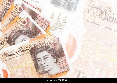 10 britische Pfund Scheine liegen im Stapel auf dem Hintergrund der großen halbtransparenten Banknote. Abstrakter Geschäftshintergrund mit Kopierbereich Stockfoto