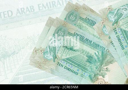 10 UAE Dirham Scheine liegt im Stapel auf dem Hintergrund der großen halbtransparenten Banknote. Abstrakte Darstellung der nationalen Währung. Geschäftskonzept Stockfoto