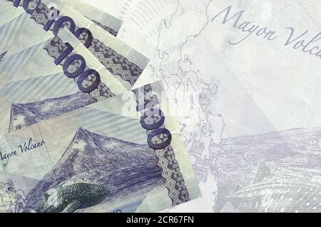 100 philippinische Piso-Scheine liegen im Stapel auf dem Hintergrund einer großen halbtransparenten Banknote. Abstrakter Geschäftshintergrund mit Kopierbereich Stockfoto