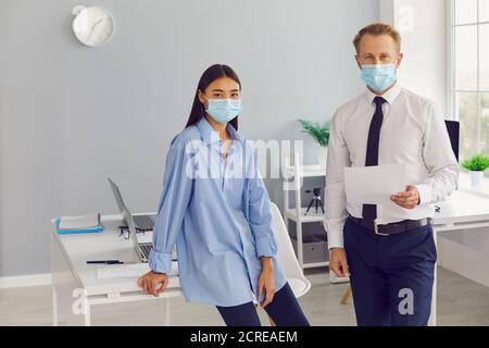 Verantwortungsvoller Mann und Frau, Arbeitnehmer des Unternehmens, trägt medizinische Gesichtsmasken bei der Arbeit Stockfoto