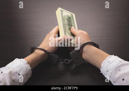 Die Hände in den Handschellen holding Papier Geld auf einem hölzernen Hintergrund Stockfoto