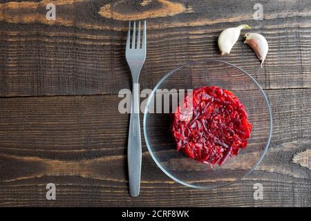 Vegetarischer Salat aus Rüben, Karotten, Knoblauch und Olivenöl auf einem Teller ist auf dem Tisch, in der Nähe von Gabel und Knoblauchzehen, Draufsicht Stockfoto