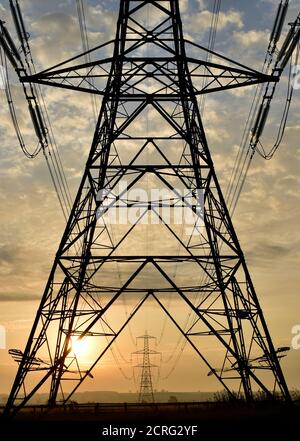 National Grid Strom Pylon Tower Struktur Silhouette bei Sonnenaufgang Framing entfernten Pylonen / Türme und Oberleitungen. Stockfoto