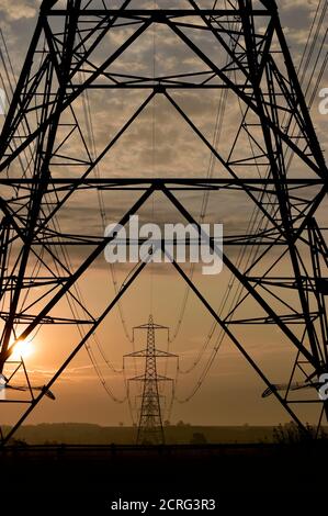 Elektrische Pylon Turm untere Hälfte Rahmen entfernten Pylonen mit elektrischen Versorgungskabeln, die zu Abstand mit atmosphärischen Sonnenaufgang am frühen Morgen Großbritannien. Stockfoto