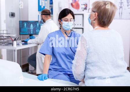 Untersuchung des Herzschlags des Patienten durch die Krankenschwester im Krankenhaus während des Coronavirus-Ausbruchs im Sprechzimmer der Klinik. Medizinische Untersuchung auf Infektionen, Krankheit und Diagnose. Stockfoto
