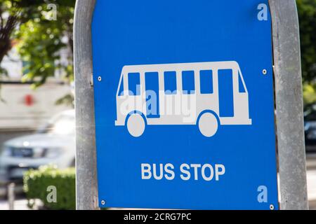 Eine blaue Tafel mit einem Bild einer Bushaltestelle mit Verkehr im Hintergrund. Städtisches Verkehrssystem. Stockfoto