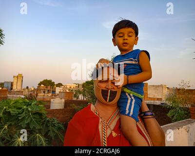 DISTRIKT KATNI, INDIEN - 21. MAI 2020: Indische kleine Kinder sitzen auf seiner Mutter Schulter am Himmel Hintergrund. Stockfoto