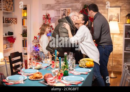 Glückliche Frau begrüßt ihren Schwiegervater zum weihnachtsessen der Familie. Stockfoto