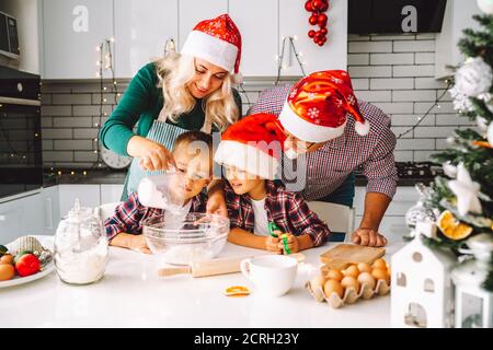 Familie von zwei Zwillingen Jungen und Alter Eltern, die Kekse für den Weihnachtsabend in der hellen Küche vorbereiten. Stockfoto