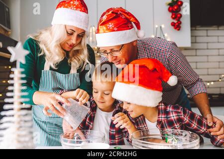 Familie von zwei Zwillingen Jungen und Alter Eltern, die Cookies vorbereiten Für Weihnachten Abend in der hellen Küche Stockfoto