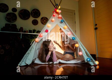 Glückliche Mutter und Tochter im Tipi Zelt im Schlafzimmer, genießen Sie reden und Geschichte erzählen; Familienbeziehung Konzept. Stockfoto