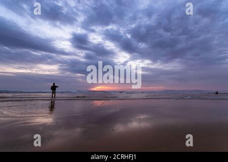 Ein junger Mann, der im offenen Meer entlang der Atlantikküste an der Costa da Caparica in Lissabon, Portugal, fischt. Attraktive Kerl hält die Fischerei ro Stockfoto