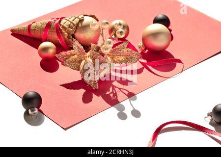 Goldene Waffel-Eiscreme-Kegel, weihnachtliche Gold- und schwarze Kugeln und Zweig mit Beere auf hellrosa Papier. Stockfoto