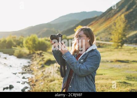 Schöne lächelnde blonde junge Frau Reisende mit Fotokamera in den Händen, Reise in die Berge Stockfoto