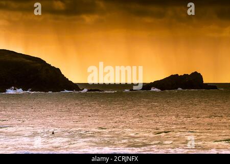 Regenwolken und ein spektakulärer feuriger Sonnenuntergang über Pentire Point East und Goose Island bei Fistral in Newquay in Cornwall. Stockfoto