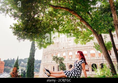 Rom, Italien - EINE junge, rothaarige brasilianerin in den Zwanzigern blickt am Nachmittag mit dem Kolosseum im Hintergrund zurück zur Kamera. Stockfoto